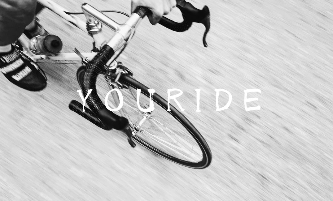 走行中の自転車のハンドルと車輪を捉えた、白いYOURIDEロゴ入りのモノクロ写真